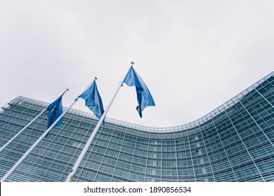The queue of steeples with blue flags of the European Union against the background of the European Commission building in Brussels, Belgium. EU flag, symbol - Shutterstock ID 1890856534