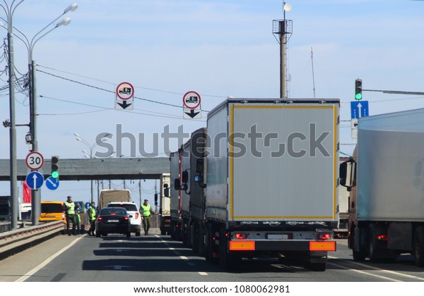 The queue of trucks with semi-trailers to the control
point in the spring against the blue sky, inspectors in yellow
jackets and camouflage check the documents of the driver of the
car
