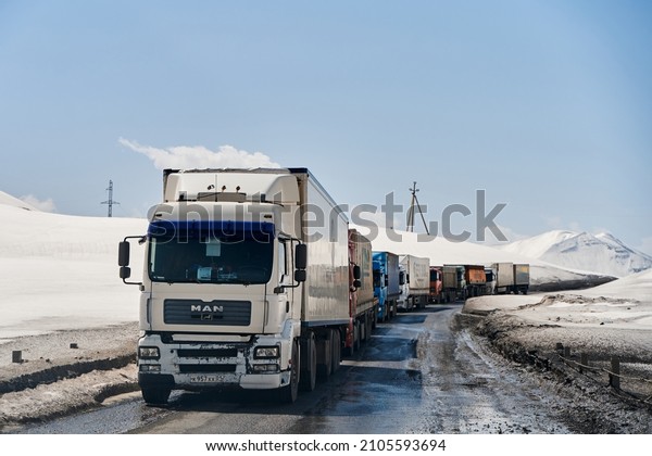 queue of trucks in the snow-capped mountains\
is waiting for the pass cleared. Transportation of goods in\
difficult weather conditions. This is why your package is delayed.\
Gudauri,Georgia -\
04.06.2021