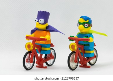 Quezon City, Philippines - February 20, 2022: Lego Simpsons Minifigure Bart Simpson as Bartman and Milhouse as Fallout Boy riding red bikes (side by side)