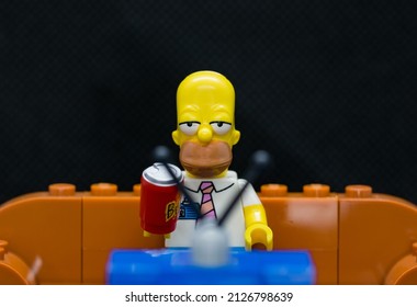 Quezon City, Philippines - February 20, 2022: Lego Simpsons Minifigure Homer Simpson watching TV while drinking soda and sitting on a couch (black background)