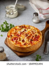Quiche of shortcrust pastry with chanterelle mushrooms and cheese with a golden brown crust on a wooden board on a gray table, close-up, near herbs and spices