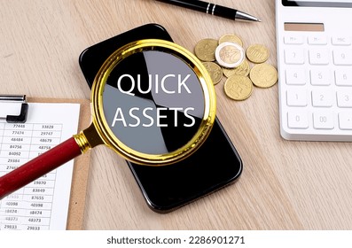 QUICK ASSETS text on magnifier with smartphone, calculator and coins