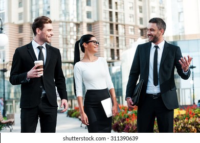 Quick Briefing Before Meeting. Three Cheerful Young Business People Talking To Each Other While Walking Outdoors