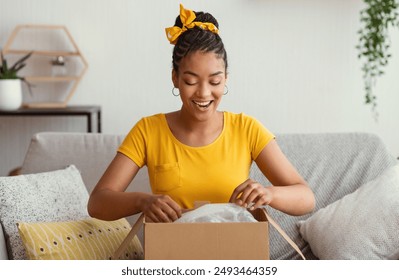 Quick Delivery Service Concept. Happy black lady received package, unpacking cardboard box, sitting on the sofa in living room at home, copy space. Female buyer satisfied with online shopping purchase - Powered by Shutterstock