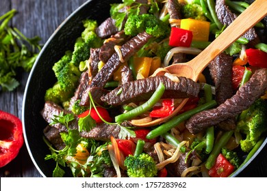 Quick And Easy Meal Steak Fajitas With Vegetables: Broccoli, Green Bean, Yellow And Red Sweet Peppers, Parsley, Onion Served On A Skillet With A Wooden Spoon On A Dark Wooden Table, Close-up