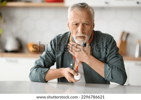 Quick Help. Senior Man Touching His Chest And Pressing Emergency Call Button, Elderly Gentleman Giving Sos Alarm Panic Call, Feeling Heart Pain While Sitting At Table In Kitchen, Free Space