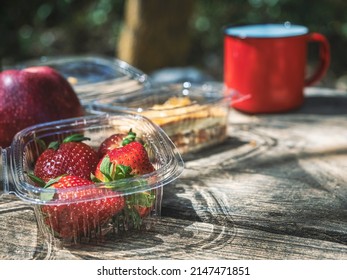 Quick Lunch In The Middle Of Nature On A Wooden Table.Strawberries, Apple, Meat Pie, Plastic Containers.One Cup.Take Away Food,outdoor Life.Copy Space