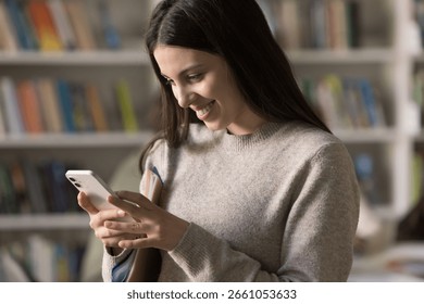 Quick message before study. Portrait smiling young female high school student hold folder with papers under arm use mobile phone in classroom check social media updates text in chat staying connected