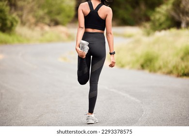 A quick warmup before her run. Rearview shot of a sporty young woman stretching her legs while exercising outdoors.