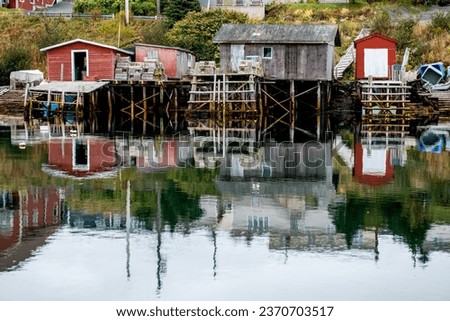 Quidi Vidi, Newfoundland, Canada: October 4, 2023: A historic fishing village with boat houses, storage sheds, colorful boats, and a slipway. The buildings are reflecting in the calm ocean water. 