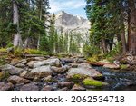 Quiet, peaceful morning at an alpine stream during sunrise with rugged peaks and scene framed by pine trees in the Rocky Mountains, Colorado, USA