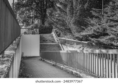 A quiet road, an approach to an underground passage under the railway line, bordered by metal fences and surrounded by trees, captured in a timeless black and white aesthetic. Stairs and fence - Powered by Shutterstock