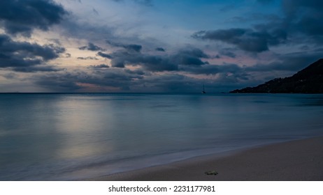 A quiet serene evening on a tropical beach. The turquoise ocean is calm. Foam on the sand . Blue clouds in a pinkish sky. Yachts on the horizon. Long exposure. Seychelles. Mahe. Beau Vallon - Shutterstock ID 2231177981