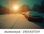 A quiet, snow-covered urban street at night, illuminated by a single streetlight, with parked cars and a residential building in the background.