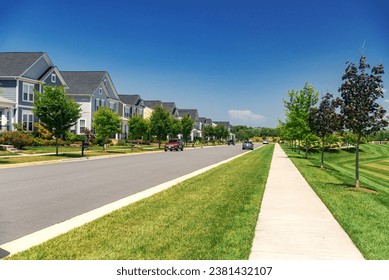 Quiet street in a residential area in the suburbs. Rows of houses along the sidewalk with a green lawn.