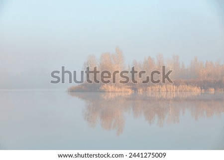 Quiet sunny foggy morning. Fog over the autumn lake at the sunrise moment.