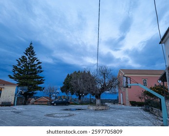 A quiet town square under a dramatic sky, featuring trees, buildings, and a basketball court.