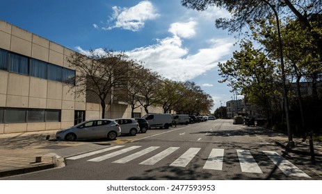 Quiet urban street with pedestrian crossing, parked vehicles, and leafless trees against a cloudy sky, suggesting off peak travel or weekend city life - Powered by Shutterstock