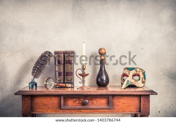 Quill ink pen with old inkwell, antique\
books, brass magnifying glass, candle in vintage candlestick,\
bottle covered with leather, carnival mask on oak wooden table.\
Retro style filtered\
photography