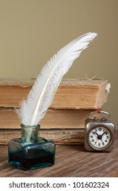 Quill and inkwell, old books, vintage clock on grunge wooden table