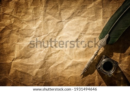 Quill pen and ink well resting on blank parchment paper background with copy space for message