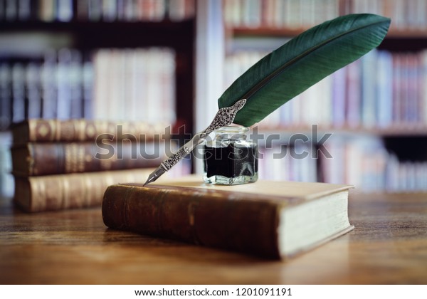 Quill pen and ink well resting on an old book in a library concept for literature, writing, author and history