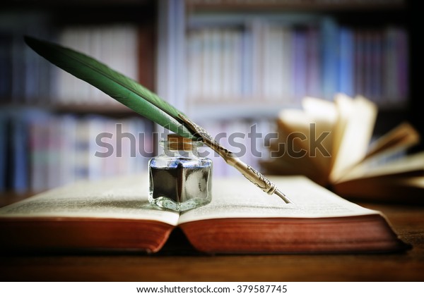 Quill pen and ink\
well resting on an old book in a library concept for literature,\
writing, author and\
history
