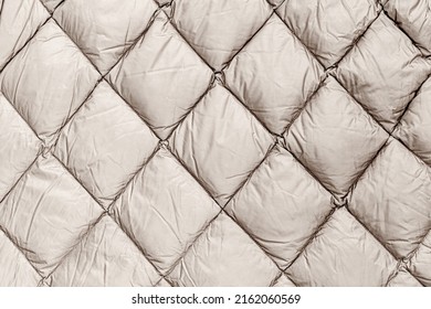 Quilted fabric backdrop. Beige quilt texture blanket or puffer jacket. Warm winter jacket with modern quilted pattern for cold winter season. Down jacket fashion background. 