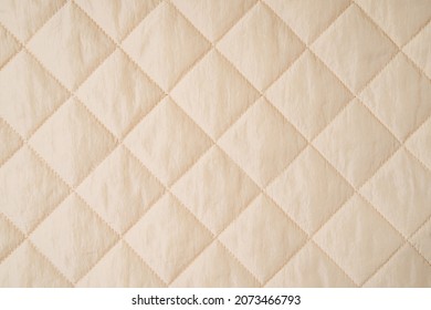 Quilted fabric background. Beige  texture blanket or puffer jacket 