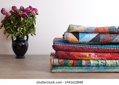 Quilts Stack And A Bouquet Of Dried Roses In A Vase On White Wall Background