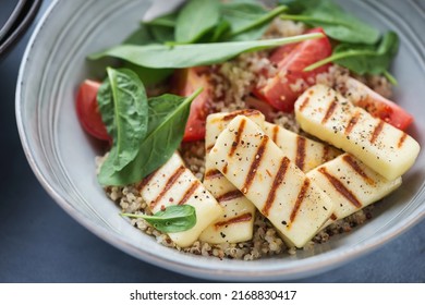 Quinoa with grilled halloumi cheese, fresh spinach and red tomatoes served in a grey bowl, closeup, selective focus