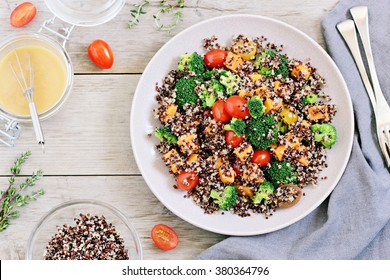 Quinoa salad with broccoli, sweet potatoes and tomatoes on a rustic wooden table. Three-color quinoa salad. Superfood and healthy eating concept. 
