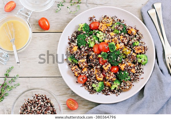 Quinoa salad with broccoli, sweet potatoes and\
tomatoes on a rustic wooden table. Three-color quinoa salad.\
Superfood and healthy eating concept.\
