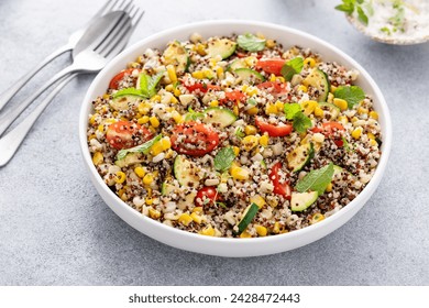 Quinoa salad with vegetables and herbs in a serving bowl with fresh tomatoes, grilled zucchini and corn - Powered by Shutterstock