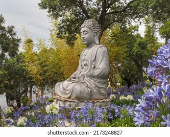 Quinta dos Loridos, Portugal - 06 18 2022: Large granite Buddha, surrounded by blue African lily or Lily of the Nile flowers, in the Bacalhôa Buddha Eden park or Garden of Peace.
