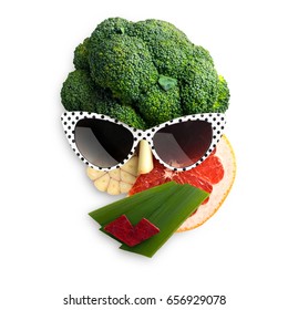 Quirky food concept of cubist style female face in sunglasses made of fruits and vegetables, on white background.