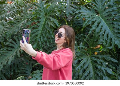 Quirky girl taking a selfie outdoors in the park with a garden plant backdrop