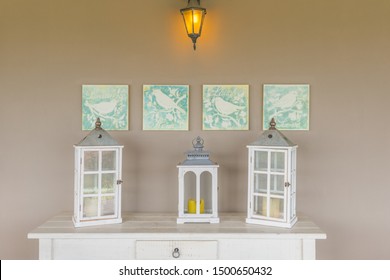 Quirky Home Decor Detail, With White Lantern Candle Holders On Top Of A White Table And A Cream Wall