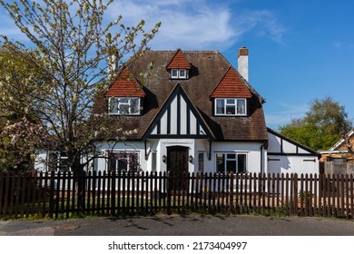 A Quirky Mock Tudor English Detached House With A Picket Fence And Tree In Blossom Against A Blue Spring Sky