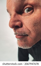 Quirky Portrait Of A Senior Man Peering At The Camera With One Eye Close Up Against The Lens In A Cropped Headshot