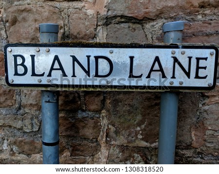 Quirky road sign for Bland Lane, against a traditional stone wall in Epperstone, UK