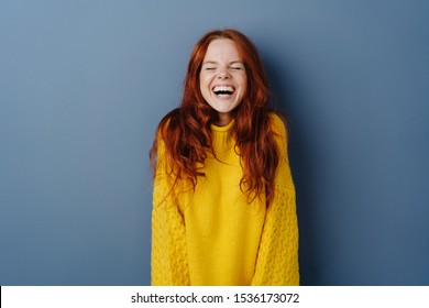 Quirky young woman screwing up her eyes as she enjoys a hearty laugh at a joke over a blue studio background with copy space
