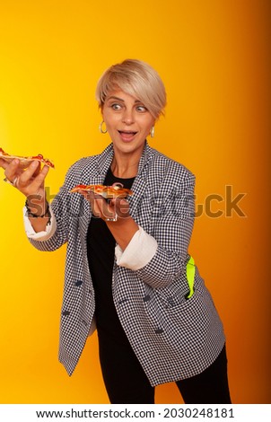 quite funny woman on a yellow background in classic clothes bites greedily a piece of pizza. junk food