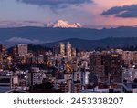 Quito buildings illuminated with the Antisana volcano in the background at dusk.
