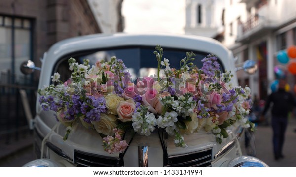 Quito, Pichincha / Ecuador - June 22 2019:\
Arrangement of red and yellow roses on the hood of an old white car\
parked on a street full of people\
walking