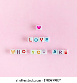 Quote "Love who you are" made out of beads on pastel pink background
