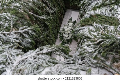 Raasiku Estonia - February 05 2022: Funeral Ceremony In Small Lutheran Graveyard. Coffin In The Grave That Is Decorated With Spruce Branches. Flower Wreath On Wooden White Chest. 