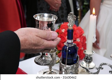 Rabbi holds kiddish cup with wine in front of Groom and Bride