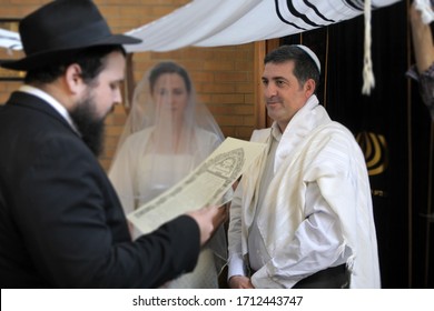 Rabbi reading the Jewish Marriage Contract (Ketubah) to Jewish bride and a bridegroom in modern Orthodox Jewish wedding ceremony in synagogue.Real people. Copy space